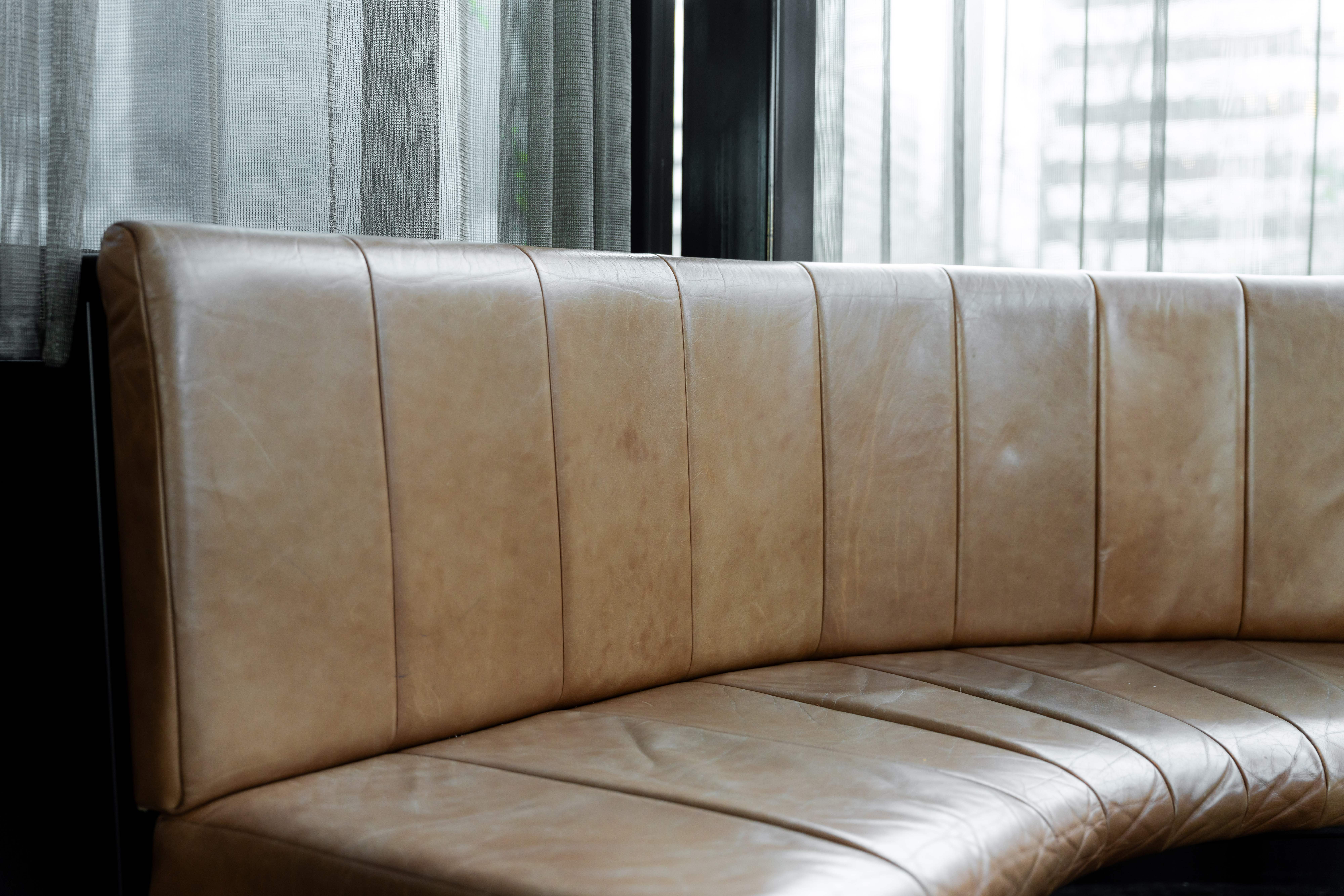 Restored tan leather channel back banquette in a venue dining room, curtains and windows behind, ready for service