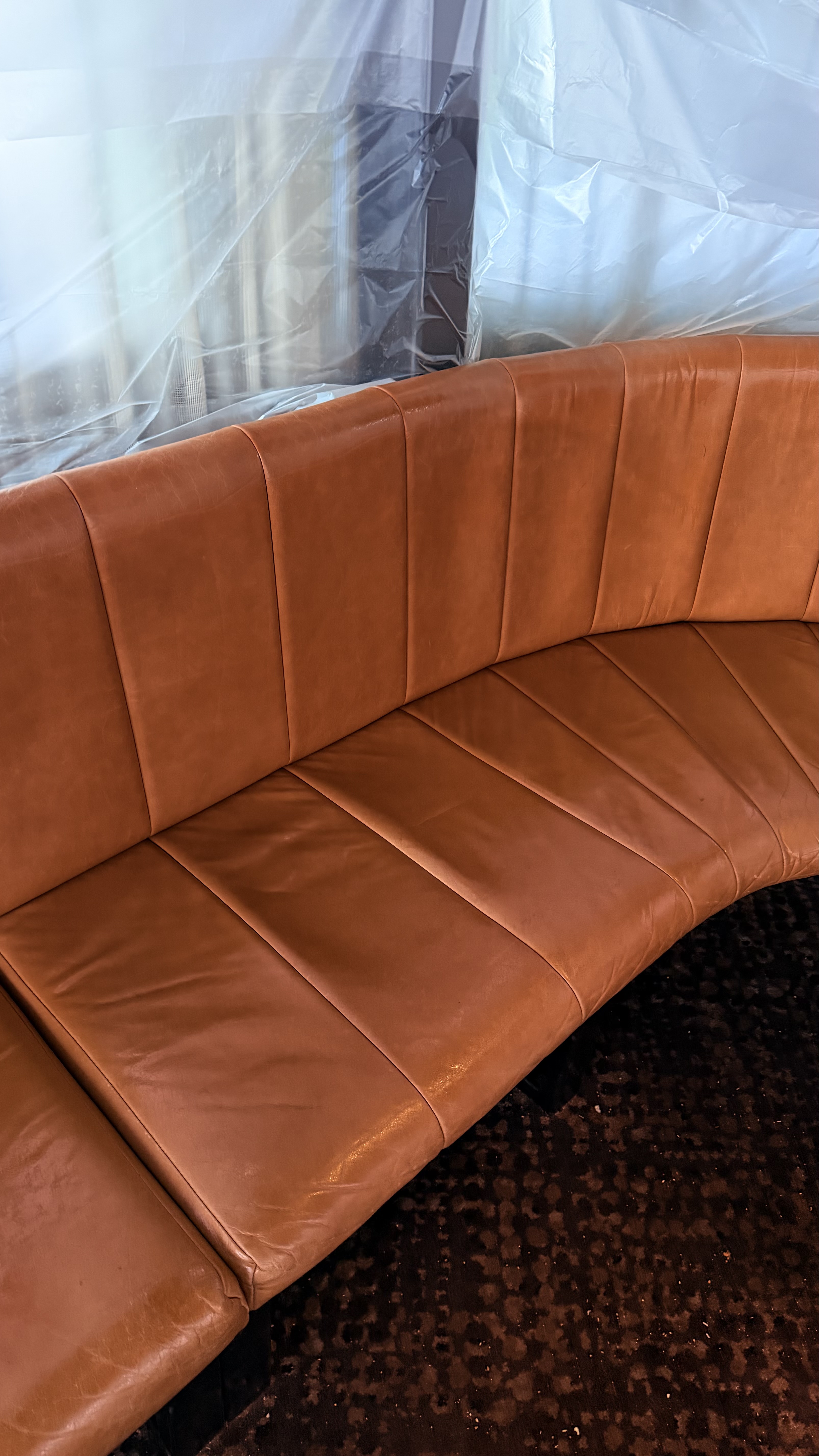 Curved tan leather channel back banquette freshly restored inside a venue, with the surrounding area sheeted off in plastic