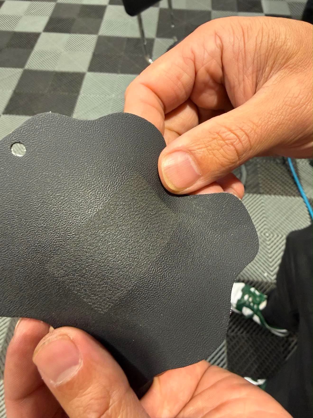 A black leather swatch held in two hands showing laser applied grain matched to the original leather texture